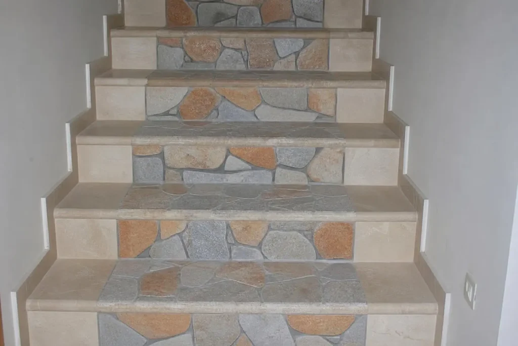 Alternance de tapis de pierre sur escalier intérieur en bordures beige et pierres gris-rouge, pose en mosaïque sur marches.