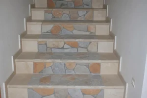 Alternance de tapis de pierre sur escalier intérieur en bordures beige et pierres gris-rouge, pose en mosaïque sur marches.